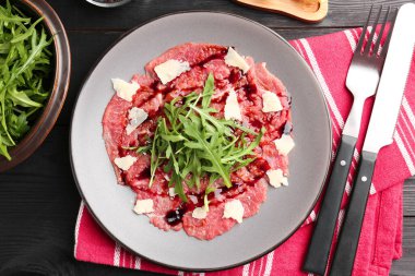 Taze et carpaccio roka, peynir ve sos siyah ahşap masada servis edilir.