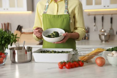 Mutfaktaki mermer masada ıspanaklı lazanya yapan kadın, yakın plan.