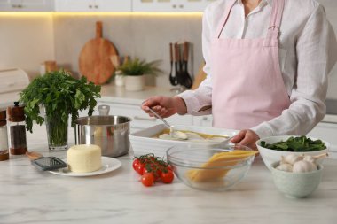 İçerideki mermer masada ıspanak lazanyasına beşamel sosu döken kadın, yakın plan.