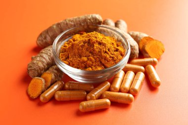 Kavanozda zerdeçal tozu, turuncu arka planda kök ve kapsüller, yakın plan.