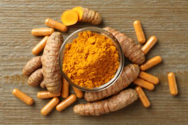 Zerdeçal kapsülleri, toz ve kökler ahşap masada, düz yerde.