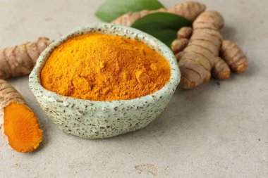 Kasede Aromatik zerdeçal tozu, taze kökler ve açık gri masadaki yapraklar, yakın plan.
