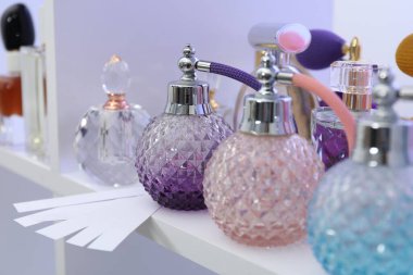 Different bottles of luxury perfume and fragrance blotters on shelf in store, closeup clipart