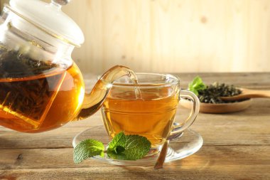 Çaydanlıktan cam fincana taze demlenmiş çay dökülüyor ahşap masada, yakın plan.