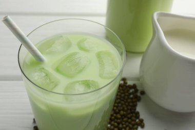 Bardakta buzlu taze fasulye suyu ve beyaz ahşap masada tohumlar, yakın plan.