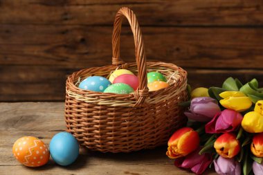 Hasır sepetteki Paskalya yumurtaları ve ahşap masada güzel laleler.