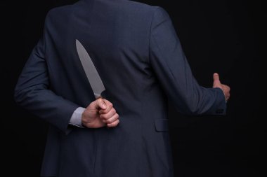Sırtında bıçak tutan bir iş adamı siyah arka planda el sıkışma teklif ediyor.