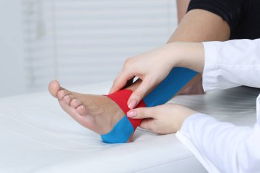Hastanedeki hastanın ayağına Kinesio bantları takan doktor.
