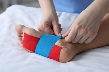 Hastanedeki hastanın ayağına Kinesio bantları takan doktor.
