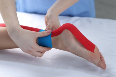 Hastanedeki hastanın ayağına Kinesio bantları takan doktor.