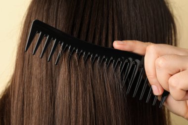 Bej arka planda plastik tarakla saçını tarayan kadın, yakın plan.