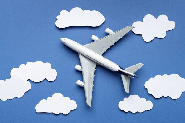Plane model flying among paper clouds on blue background, flat lay