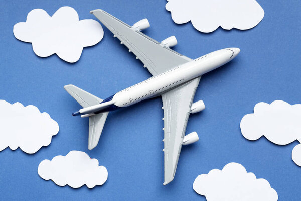Plane model flying among paper clouds on blue background, flat lay