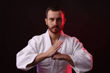 Karate dövüşçüsü siyah arkaplan karşısında renk ışığı altında üniforma giyiyor.