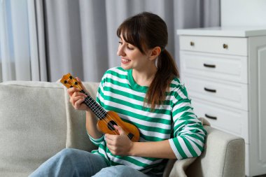 Evdeki kanepede ukulele çalan mutlu kadın.
