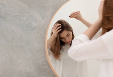 Saç dökülme problemi. Banyoda aynanın yanındaki saç çizgisine serum uygulayan bir kız. Mesaj için yer var.