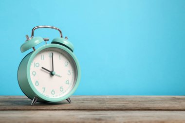 Açık mavi arkaplan ile ahşap masa üzerinde bir turkuaz alarm saati, metin için boşluk