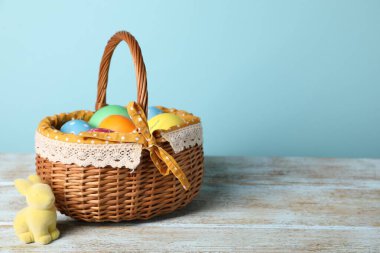 Hasır sepetteki güzel Paskalya yumurtaları ve ahşap masadaki tavşancık figürü açık mavi arkaplan, metin için alan