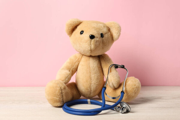 Pediatrics concept. Teddy bear with stethoscope on wooden table against pink background