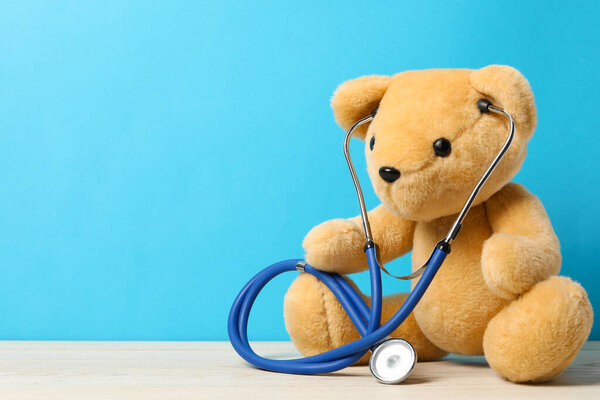 Pediatrics concept. Teddy bear with stethoscope on wooden table against light blue background, space for text