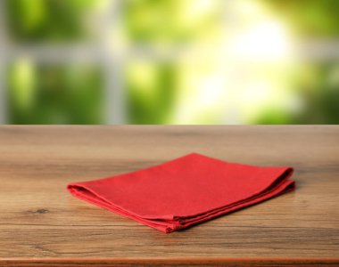 Odasındaki ahşap masanın üzerindeki kırmızı masa örtüsü, bulanık güneş ışığına karşı, yakın plan.