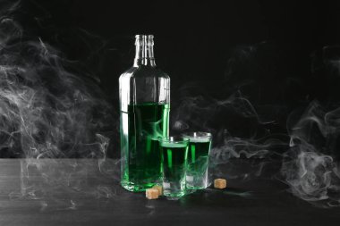Absinthe shot bardakları, şişe ve esmer şeker siyah arka planda dumanlı