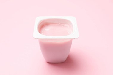 Açık pembe arka planda plastik bardakta lezzetli yoğurt, yakın plan.