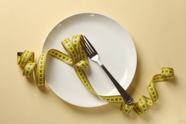 Bulimia. Bej arka planda çatal ve mezura ile plaka, üst görünüm