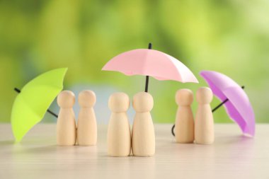 Şemsiyelerin altındaki insan figürleri açık havada, açık ahşap masada. Sigorta konsepti