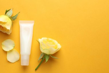 Sarı arka planda dudak kremi ve güller, düz yatış. Metin için boşluk