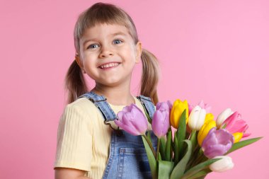 Gülümseyen küçük kız pembe arka planda bir buket laleyle