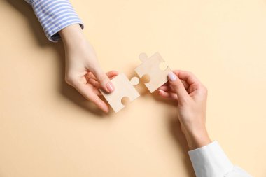 İş stratejisi ve takım çalışması konsepti. Ortaklar, bej arkaplan ve üst görünüm üzerine yapboz parçaları koyuyorlar