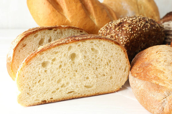 Whole and cut bread loafs on white table, closeup