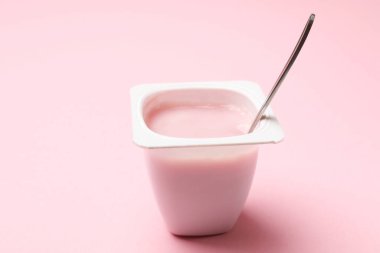 Plastik bardakta lezzetli yoğurt açık pembe arka planda kaşık, yakın plan.