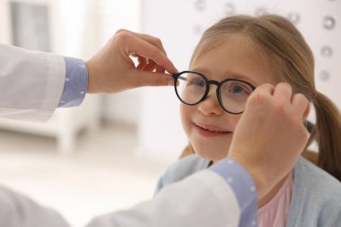 Vizyon testi. Oftalmolog küçük kıza gözlük veriyor, yakın plan.