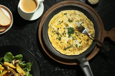 Lezzetli bir kahvaltı. Lezzetli omlet, kızarmış patates ve siyah desenli masada servis edilen kahve.