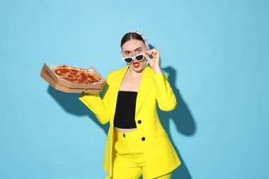 Açık mavi arka planda lezzetli pizzası olan şık bir kadın.