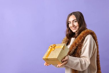 Mor arka planda süs ve hediye kutusu olan mutlu genç bir kadın. Metin için boşluk