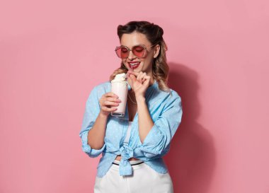 Pembe arka planda milkshake 'i olan mutlu kadın.