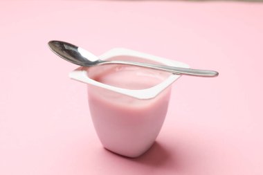 Plastik bardakta lezzetli yoğurt açık pembe arka planda kaşık, yakın plan.