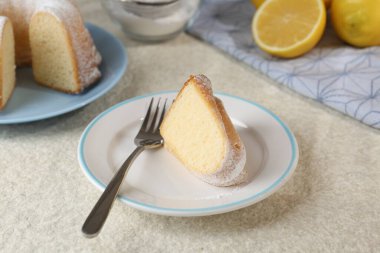 Bir parça leziz limonlu kek, pudra şekeri ve çatalla ince desenli masa, yakın plan.