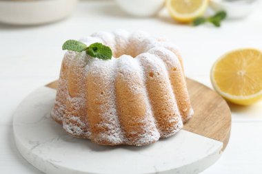 Beyaz ahşap masada pudra şekerli, nane ve narenciye meyveli lezzetli limonlu pasta, yakın plan.