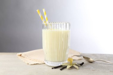 Bir bardak süt, vanilya kabuğu, çiçek ve kaşık açık gri masada.