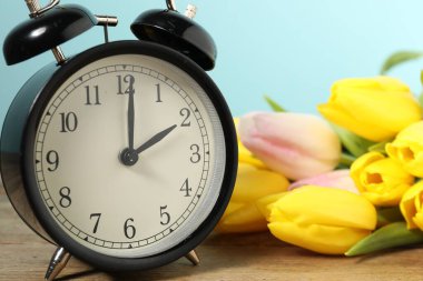 Bahar geldi. Alarm saati ve ahşap masanın üzerindeki güzel laleler açık mavi arka plan, yakın plan