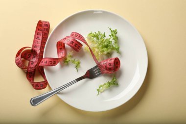 Bulimia. Bej arka planda marul, çatal ve mezura ile plaka, üst görünüm