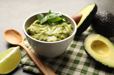 Lezzetli avokado sosu, maydanoz ve meyveler gri masada, yakın plan.