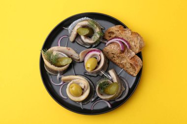 Sarı masada zeytinli, turşulu, dereotlu, soğanlı ve ekmekli lezzetli ringa dürümleri.