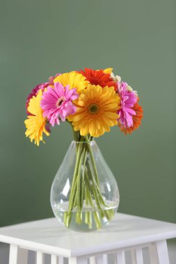 Bir buket güzel Gerbera çiçeği, cam vazoda, beyaz masada.