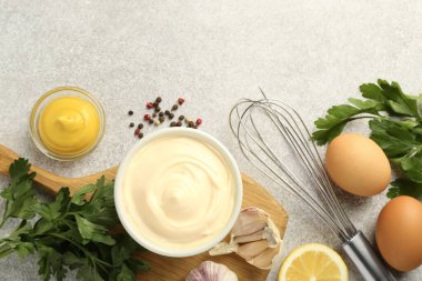 Lezzetli mayonez sosu kasede, çırpı ve malzemeler gri masada, düz yerde.