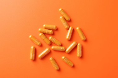 Turuncu arka planda zerdeçal kapsülleri düz.